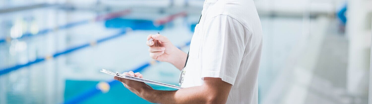 Mann steht im Schwimmbad mit einem Klemmbrett und Stift